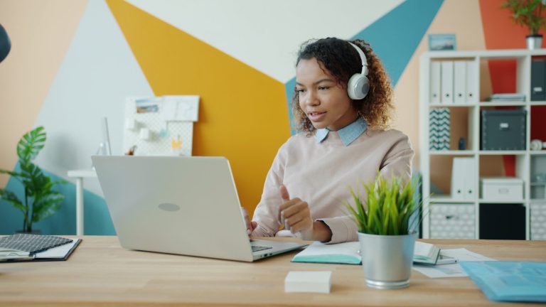 A woman wearing headphones is working on a laptop at a desk.